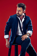 Image showing Male beauty concept. Portrait of a fashionable young man with stylish haircut wearing trendy suit posing over red background.