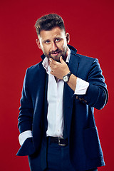 Image showing Male beauty concept. Portrait of a fashionable young man with stylish haircut wearing trendy suit posing over red background.