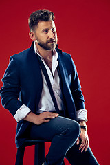 Image showing Male beauty concept. Portrait of a fashionable young man with stylish haircut wearing trendy suit posing over red background.