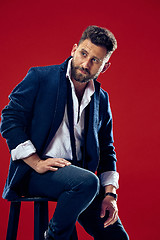 Image showing Male beauty concept. Portrait of a fashionable young man with stylish haircut wearing trendy suit posing over red background.