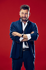 Image showing Male beauty concept. Portrait of a fashionable young man with stylish haircut wearing trendy suit posing over red background.