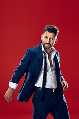 Image showing Male beauty concept. Portrait of a fashionable young man with stylish haircut wearing trendy suit posing over red background.