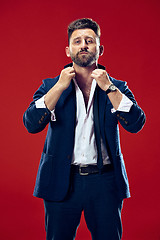 Image showing Male beauty concept. Portrait of a fashionable young man with stylish haircut wearing trendy suit posing over red background.