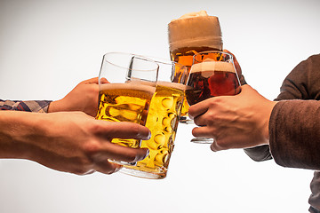 Image showing hands with mugs of beer toasting creating splash isolated on white background
