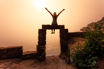 Image showing Female sitting on ancient sandstone doorway with foggy sunrise