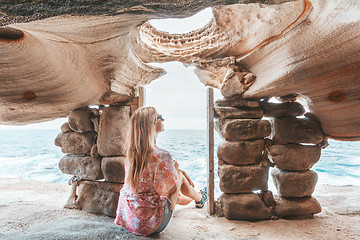 Image showing Female sits inside cliff top cave watching the ocean