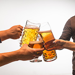 Image showing hands with mugs of beer toasting creating splash isolated on white background