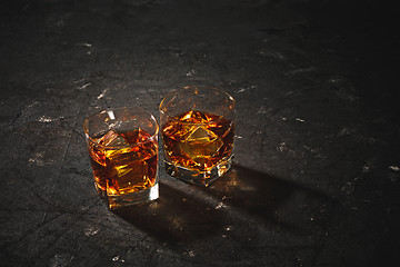 Image showing Whiskey in glass, ice cub served in a short glass on black table