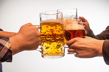 Image showing hands with mugs of beer toasting creating splash isolated on white background