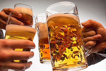 Image showing hands with mugs of beer toasting creating splash isolated on white background