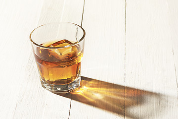 Image showing Whiskey in glass, ice cub served in a short glass on white table