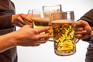 Image showing hands with mugs of beer toasting creating splash isolated on white background