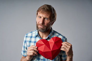 Image showing Unhappy mature man in checkered shirt holding heart shape