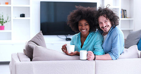 Image showing multiethnic couple sitting on sofa at home drinking coffe