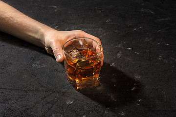 Image showing Whiskey in glass, ice cub served in a short glass on black table