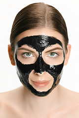 Image showing Young beautiful woman applying a mask for the face of the therapeutic black mud. Spa treatment