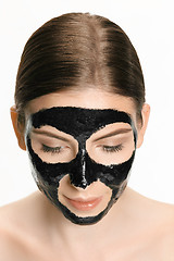 Image showing Young beautiful woman applying a mask for the face of the therapeutic black mud. Spa treatment