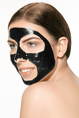 Image showing Young beautiful woman applying a mask for the face of the therapeutic black mud. Spa treatment