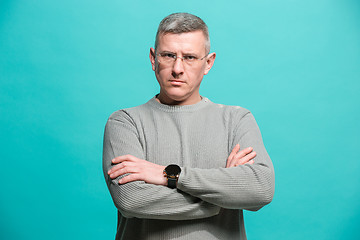 Image showing The serious businessman standing and looking at camera against blue background.