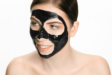 Image showing Young beautiful woman applying a mask for the face of the therapeutic black mud. Spa treatment