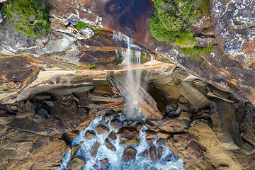 Image showing Clifftop woman sitting by the edge of waterfall tumbling into ocean