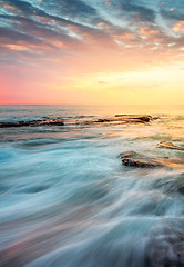 Image showing Incoming waves wash over rocks at sunrise