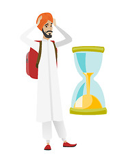 Image showing Worried hindu traveler man looking at hourglass.