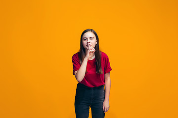 Image showing The young teen girl whispering a secret behind her hand over orange background