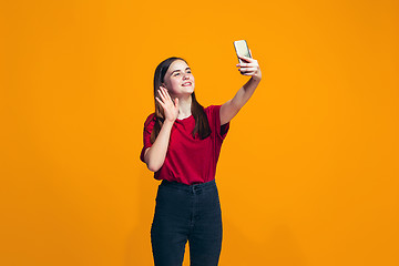 Image showing The happy teen girl standing and smiling against orange background.