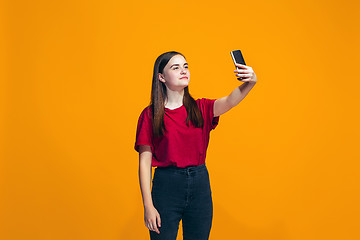 Image showing The happy teen girl standing and smiling against orange background.