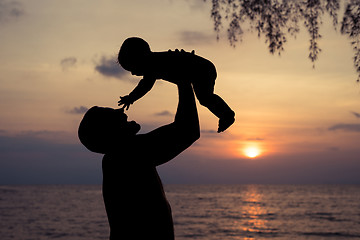 Image showing Father and baby son  playing on the beach at the sunset time.