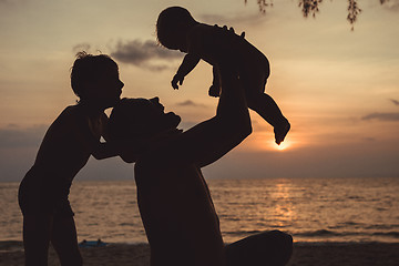 Image showing Father and two sons  playing on the beach at the sunset time.