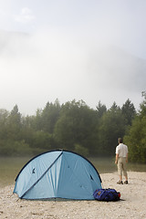 Image showing Backpacker standing beside his tent