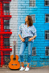 Image showing smiling woman in jeans and a blue shirt stands against the wall 