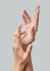 Image showing Closeup of beautiful woman hands with light manicure on nails on a gray background. Massage of hands using cream.