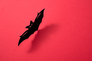 Image showing Handcraft paper bat on a red background with shadow and copy space for text. Layout to Halloween. Flat lay