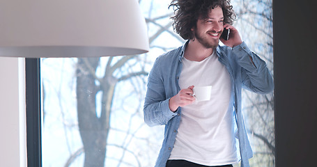 Image showing young man drinking coffee and using a mobile phone  at home