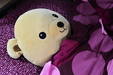Image showing Bear doll sleeping on the purple bed 