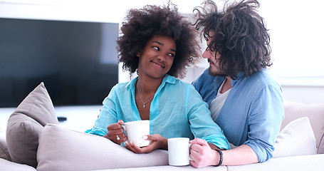Image showing multiethnic couple sitting on sofa at home drinking coffe