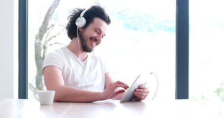 Image showing young man listenig music on tablet at home