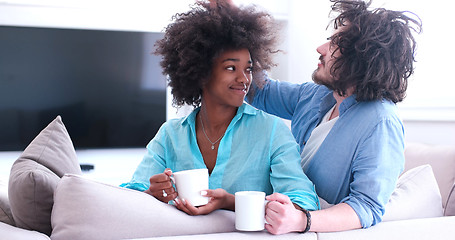 Image showing multiethnic couple sitting on sofa at home drinking coffe