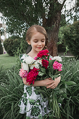 Image showing Portrait of smiling beautiful teenage with bouquet of daisies, against green of summer park.