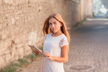 Image showing beautiful young woman in white dress using tablet