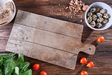 Image showing Wooden board on the kitchen table around boiled quail eggs in a bowl, pieces of nuts, tomatoes, meat and greens. Copy space. Ingredients for Healthy Salad. Flat lay