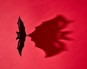 Image showing Mystical card made of hand craft paper bat with a pattern from a shadow on a red background with copy space for text. Halloween. Flat lay