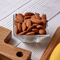 Image showing Close-up of almond nuts in a glass bowl on a wooden board on a gray wooden background. Vegetable protein for vegans.