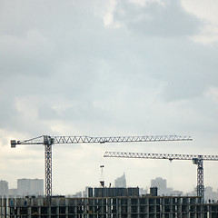 Image showing Construction cranes against the background cityscape and cloudy sky. Aerial photo from the drone.