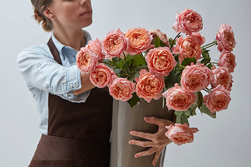 Image showing Girl florist with a big bouquet of pink roses around a gray background. The concept of a flower shop