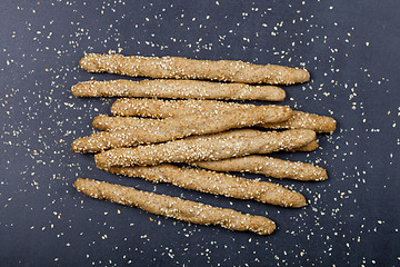 Image showing Italian grissini or salted bread sticks with sesame seeds on bla