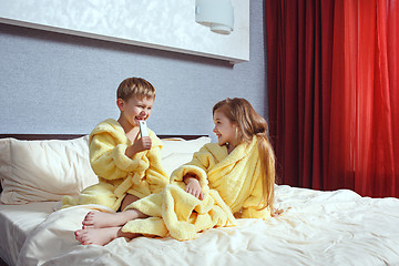 Image showing Happy laughing kids, boy and girl in soft bathrobe after bath play on white bed